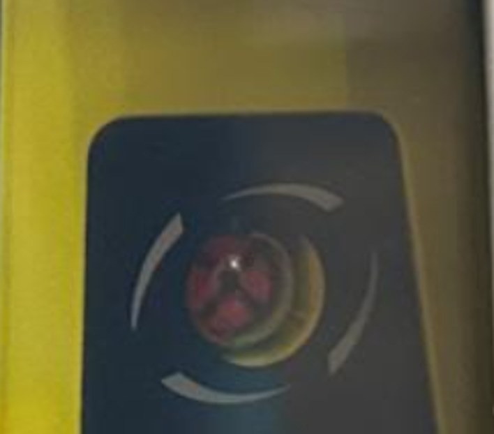 Close-up of a dime-sized red AED status indicator showing a failed self-test, viewed through cabinet glass